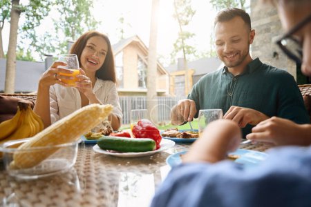 Téléchargez les photos : Maman, papa et fils déjeuner sur la terrasse d'une maison de campagne, délicieux aliments et jus sur la table - en image libre de droit