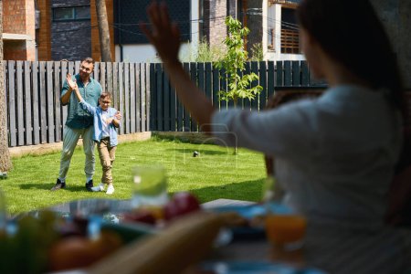 Photo for Dad and son play on the lawn near the house, mom waves to them from the terrace - Royalty Free Image
