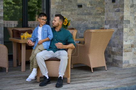 Photo for Father and his teenage son are sitting on the terrace of a country house, they are having a nice conversation - Royalty Free Image