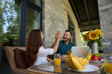 Photo for Female and male high-five each other at the table, there are fruits and sunflowers on the table - Royalty Free Image