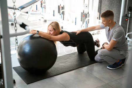 Photo for Expectant mother performs relaxing exercises for her back with a fitball, she is helped by a specialist - Royalty Free Image
