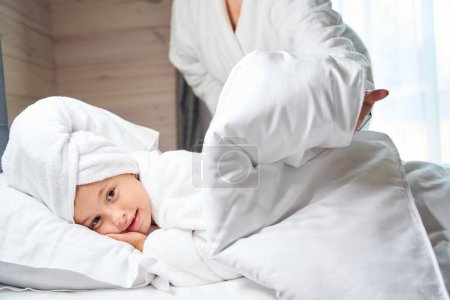 Photo for Mother covering her pretty sweet daughter in bathrobe with warm blanket, bed time, girl going to sleep after day in spa with mother - Royalty Free Image