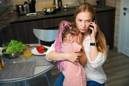 Photo for Anxious woman worrying about her little daughter who feeling sick, hugging and calming down child and calling emergency service - Royalty Free Image