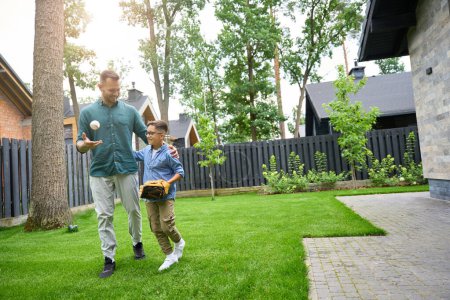 Foto de Hombre y un niño están caminando por la hierba verde cerca de la casa, el niño lleva un guante de béisbol - Imagen libre de derechos