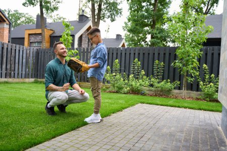 Téléchargez les photos : L'homme et son fils jouent au baseball sur la pelouse de la maison, le garçon étreint son père - en image libre de droit