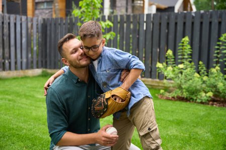 Foto de Padre e hijo juegan béisbol en el césped de la casa, el niño abraza a su padre - Imagen libre de derechos