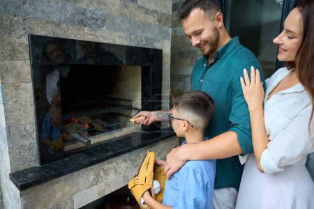 Téléchargez les photos : Garçon regarde son père cuisiner la nourriture sur le feu, à côté de leur charmante mère - en image libre de droit