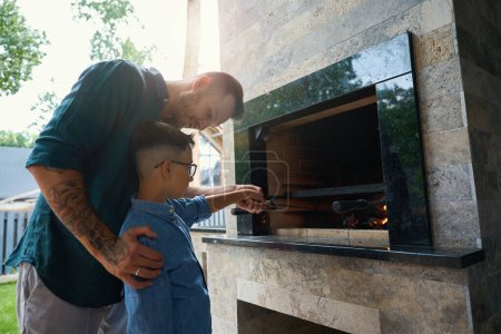 Téléchargez les photos : L'homme et son fils cuisinent au-dessus d'un feu sur la terrasse, le poêle est décoré de pierre décorative - en image libre de droit