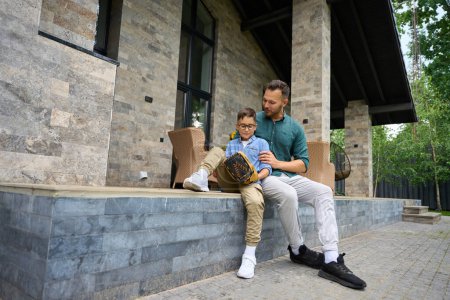 Photo for Young father communicates with his son on the terrace of a country house, the boy has a baseball gadget - Royalty Free Image