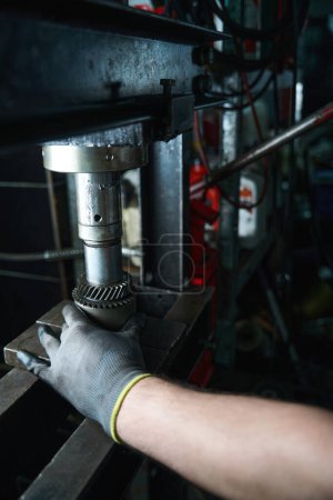 Foto de Primer plano de la mano masculina en el guante colocando el componente de metal del coche en la placa dentro de la prensa hidráulica manual - Imagen libre de derechos