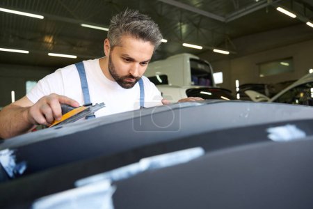 Photo for Serious focused service station worker buffing auto bumper cover with sanding block - Royalty Free Image