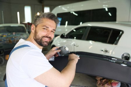 Photo for Portrait of cheerful car detailer applying layer of putty to bumper cover with trowels - Royalty Free Image