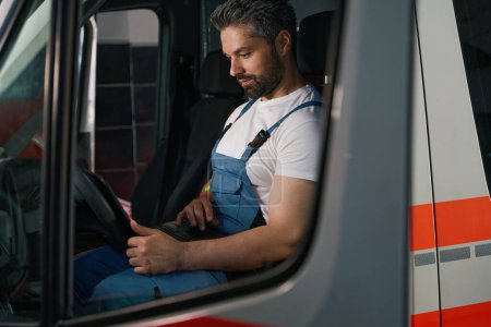 Foto de Técnico automotriz enfocado mirando la pantalla del ordenador portátil mientras está sentado en el vehículo cliente - Imagen libre de derechos
