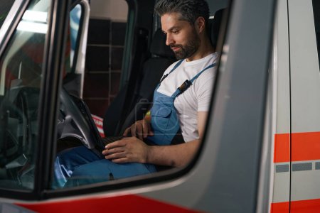 Foto de Mecánico auto concentrado mirando la pantalla del ordenador portátil mientras está sentado en el coche del cliente - Imagen libre de derechos