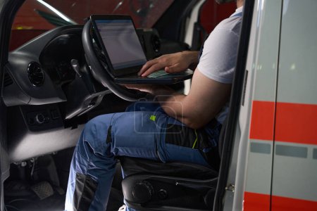 Téléchargez les photos : Photo recadrée d'un technicien de véhicule assis dans une voiture de client tapant sur un ordinateur portable dans sa main - en image libre de droit