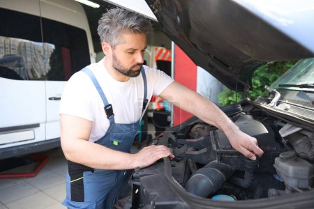 Foto de Mecánico serio enfocado en ropa de trabajo quitando la tapa del tanque de aceite del motor del coche bajo capucha abierta - Imagen libre de derechos