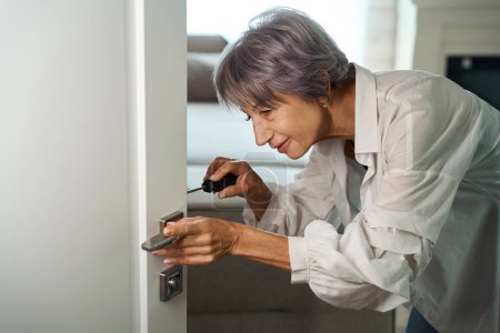 Foto de Dama con el pelo lila repara una puerta por sí misma, ella utiliza un destornillador - Imagen libre de derechos
