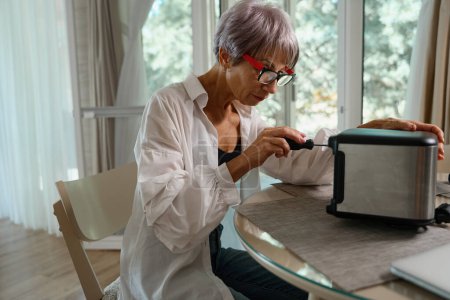 Frau mit Brille repariert am Küchentisch einen Toaster, sie benutzt einen Schraubenzieher