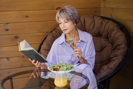 Téléchargez les photos : Femme en vêtements lilas assis sur la terrasse avec un livre et de la nourriture légère - en image libre de droit