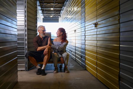 Photo for Husband and wife sat down to rest on a cargo cart, they are in a warehouse - Royalty Free Image