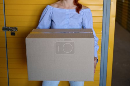 Photo for Woman stands with a cardboard box near a yellow door, there is a lock on the door - Royalty Free Image
