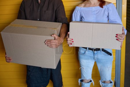 Téléchargez les photos : Femme et homme sont debout près d'un conteneur jaune, ils tiennent des boîtes en carton dans leurs mains - en image libre de droit