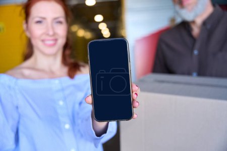 Photo for Red-haired woman has a mobile phone in her hands, she and her husband are in a warehouse - Royalty Free Image
