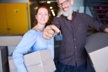Photo for Smiling people stand with boxes of things in a warehouse, a man has a lock in his hands - Royalty Free Image