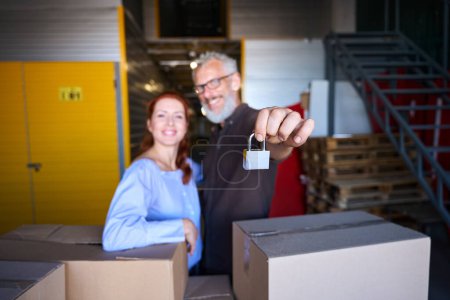 Téléchargez les photos : Les conjoints se tiennent près des boîtes avec des choses dans un entrepôt, l'homme a un cadenas dans ses mains - en image libre de droit