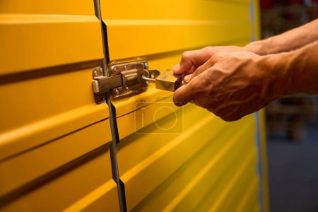 Photo for Male closes the yellow metal door with a lock, this is a modern storage room - Royalty Free Image