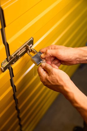 Téléchargez les photos : Homme ferme la porte en métal jaune avec une serrure, c'est une salle de stockage moderne - en image libre de droit