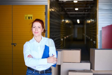Photo for Charming woman stands with a blue folder near a cargo trolley, she is in casual clothes - Royalty Free Image
