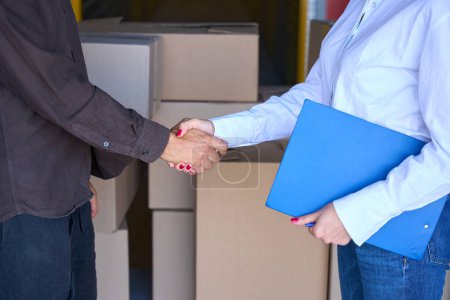 Photo for Lady with blue folder shakes hand with man, people are in warehouse - Royalty Free Image