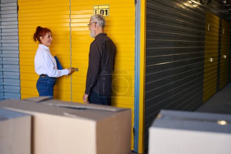 Téléchargez les photos : Femme avec un dossier bleu ouvre une porte jaune, à côté d'un homme barbu aux cheveux gris - en image libre de droit