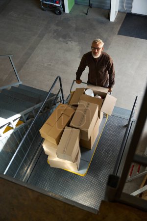 Photo for Man lifts a cart with things on a freight elevator, there are a lot of cardboard boxes on the cart - Royalty Free Image