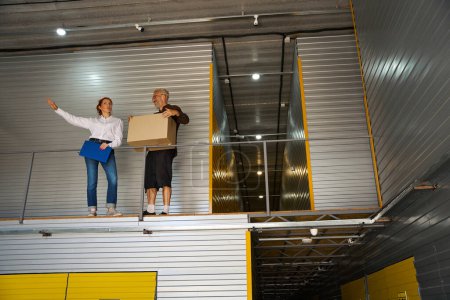 Photo for Client with the box and manager are on the second floor of the warehouse, the woman has a blue folder - Royalty Free Image