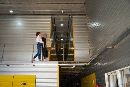 Téléchargez les photos : Un homme avec une boîte et une femme marchent dans l'entrepôt, ils sont au deuxième étage - en image libre de droit