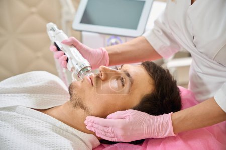 Photo for Specialist does RF face lift to a young man, the doctor uses a modern device - Royalty Free Image