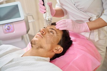 Foto de El hombre se somete a un procedimiento de elevación facial RF, el médico trabaja con el área de la frente - Imagen libre de derechos