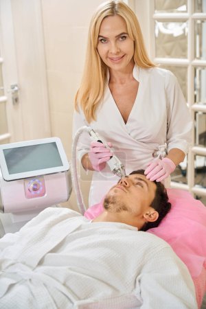 Foto de Cliente de una clínica de cosmetología se somete a un procedimiento de lifting facial RF, el médico trabaja con el área de la frente - Imagen libre de derechos