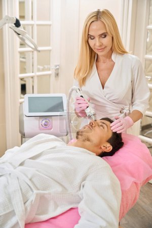 Foto de Cliente de una clínica de cosmetología que se somete a un procedimiento de elevación de la cara de microneedle RF, el médico trabaja con el área de la frente - Imagen libre de derechos