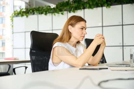 Photo for Tired woman is sitting at her workplace, in front of her is a laptop and a glass of water - Royalty Free Image