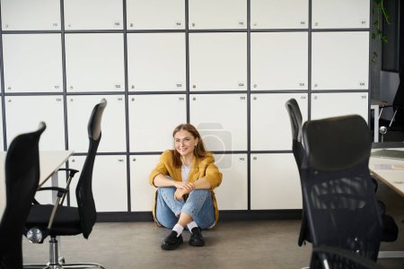 Téléchargez les photos : Gestionnaire se repose dans le bureau de coworking, elle est située sur le sol près des casiers de stockage - en image libre de droit
