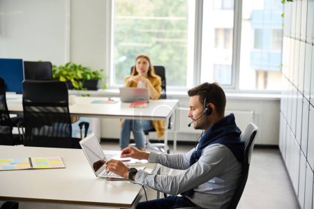 Foto de Los gerentes con computadoras portátiles en sus lugares de trabajo se comunican mediante un auricular, hay una gran ventana en la habitación - Imagen libre de derechos