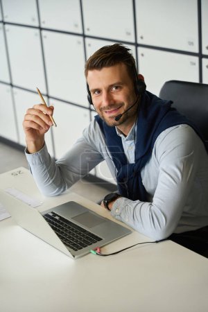 Foto de El hombre con portátil se encuentra en el área de oficina de un espacio de coworking, tiene un lápiz y un auricular - Imagen libre de derechos