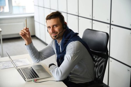 Foto de El empleado se encuentra en el área de oficina de un espacio de coworking, tiene un lápiz y un auricular - Imagen libre de derechos