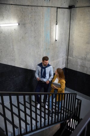 Téléchargez les photos : Femme et homme regardent à travers les documents de travail dans les escaliers du foyer, la femme a un ordinateur portable - en image libre de droit