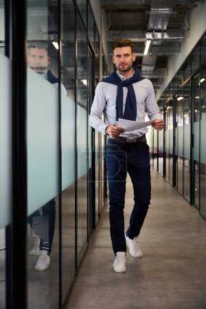 Photo for Man walks along an office corridor with work documents, he is in comfortable casual clothes - Royalty Free Image
