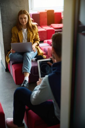Téléchargez les photos : Femme et un homme assis avec leurs ordinateurs portables sur un canapé multicolore dans un intérieur élégant - en image libre de droit