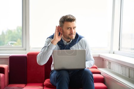 Téléchargez les photos : Homme en tenue décontractée avec un ordinateur portable dans un espace de coworking, il écoute quelque chose - en image libre de droit